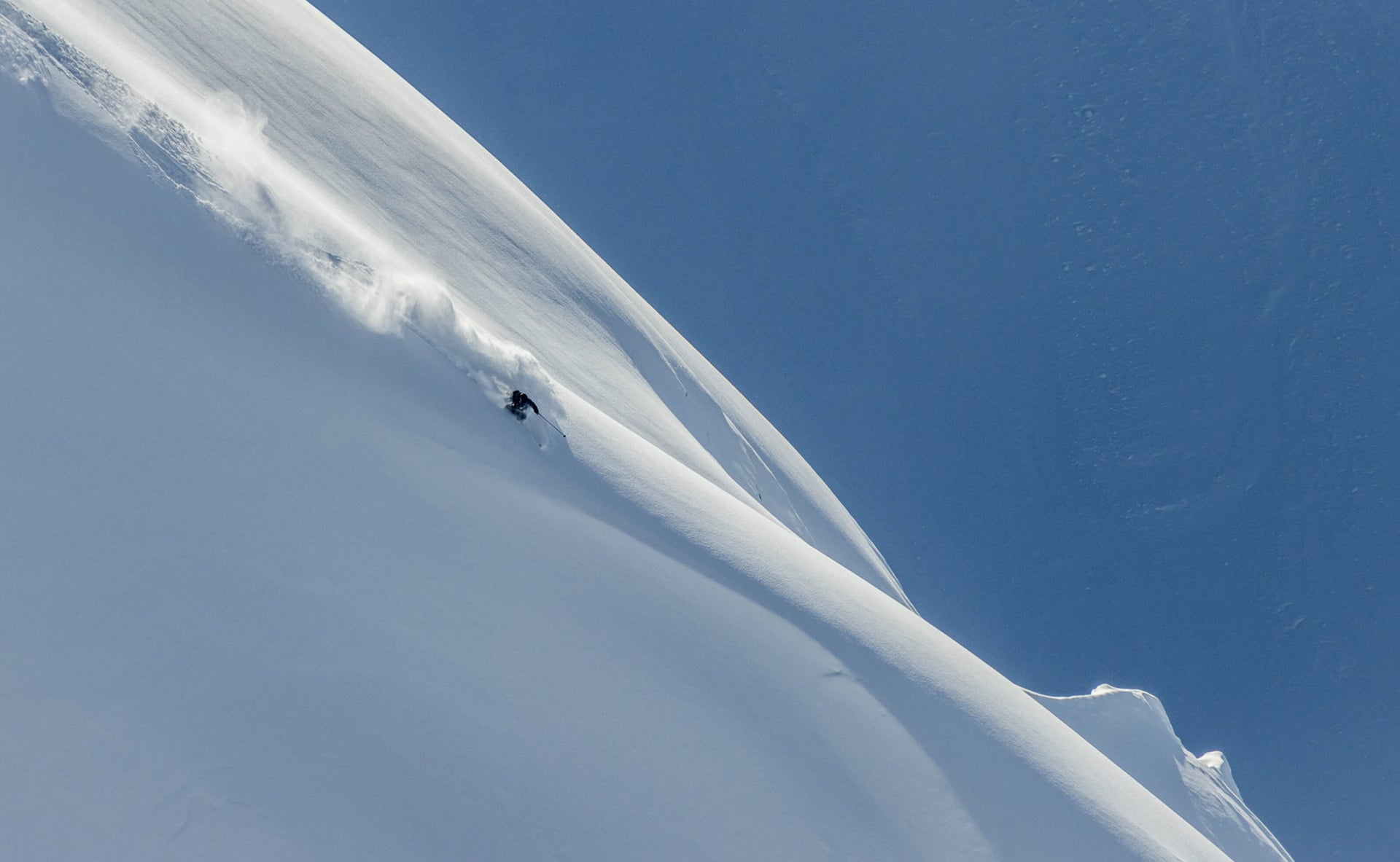 Skier slashing a pow turn on a big alpine line